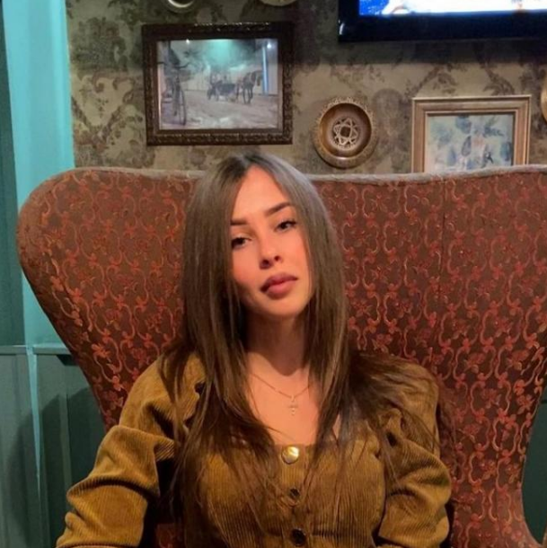 Woman sitting on a patterned chair in a room with decorative wall art.