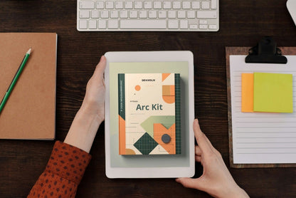 Person holding a tablet with 'Arc Kit' on screen over a desk with a keyboard and stationery items.