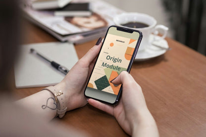 Person holding a smartphone with an app interface on a wooden table with a notebook and coffee cup.
